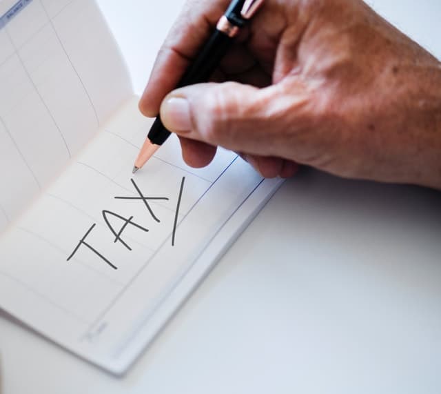 A pad with tax written on it with a hand holding a pen above it.